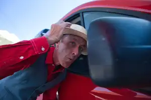 Comédien en veste rouge penché à la portière d’une voiture rouge, reportage La compagnie de l’Arrozoir